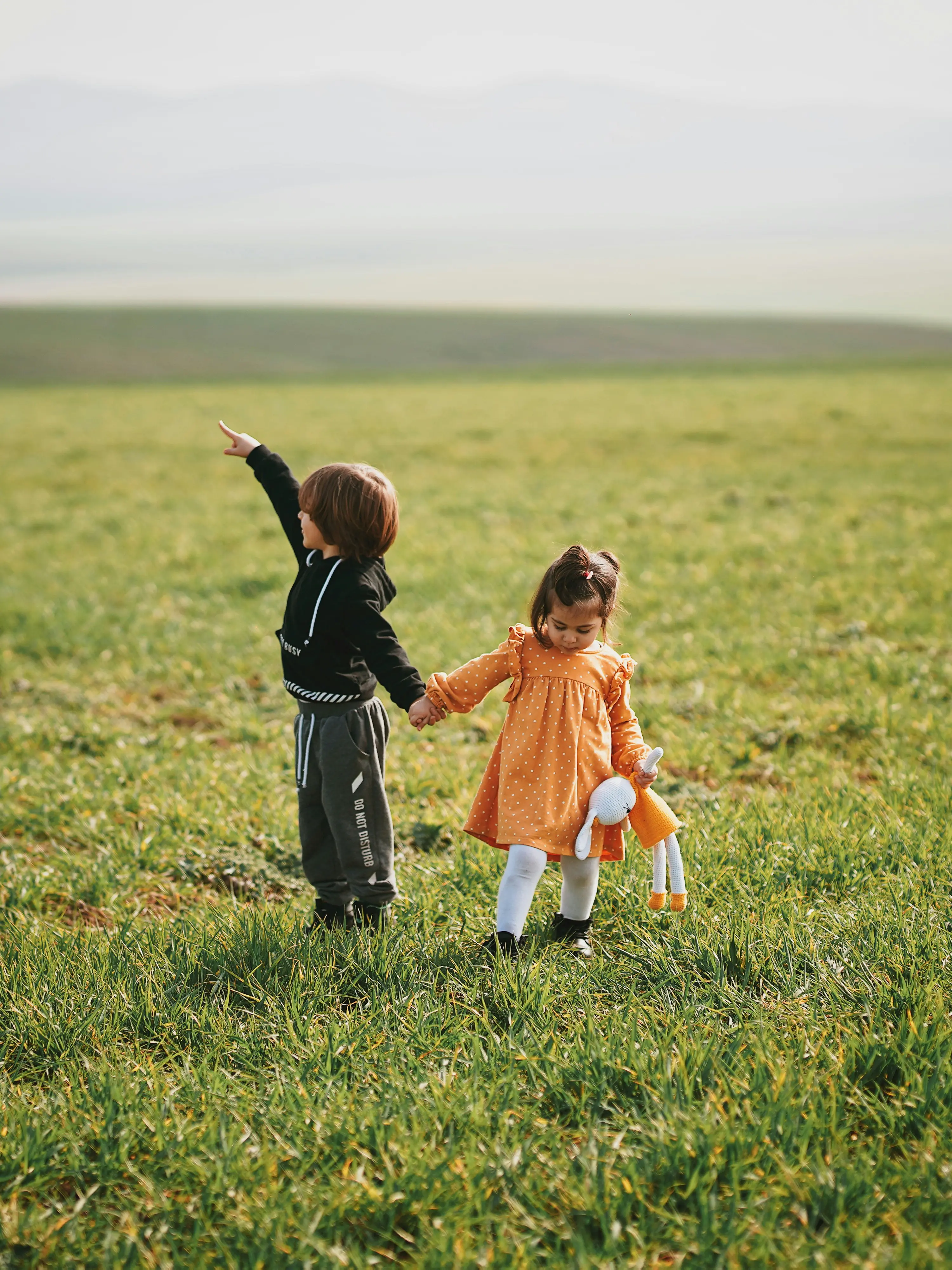 Zwei Kinder halten sich auf einem grünen Feld an der Hand, ein Kind zeigt nach links.